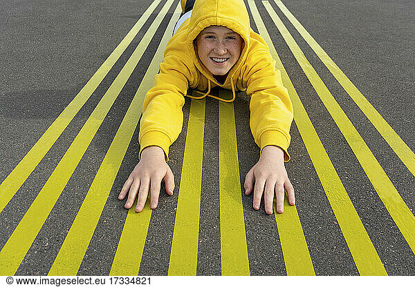 Smiling boy lying on striped yellow road markings