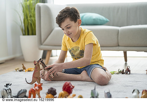 Smiling boy playing with toy animals in living room at home