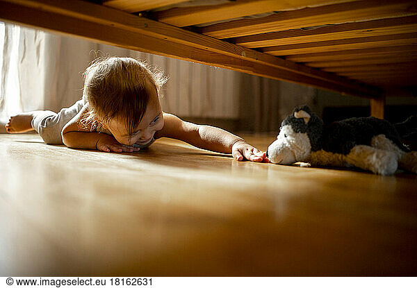 Smiling boy reaching for stuffed toy under bed at home