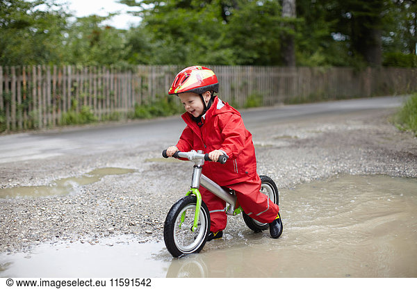 Smiling boy riding bicycle in puddles