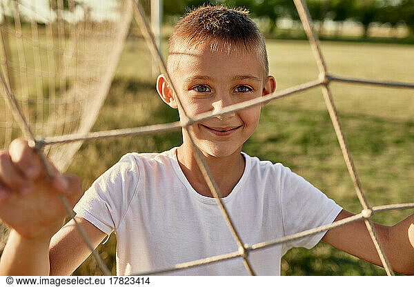 Smiling boy seen through net on sunny day