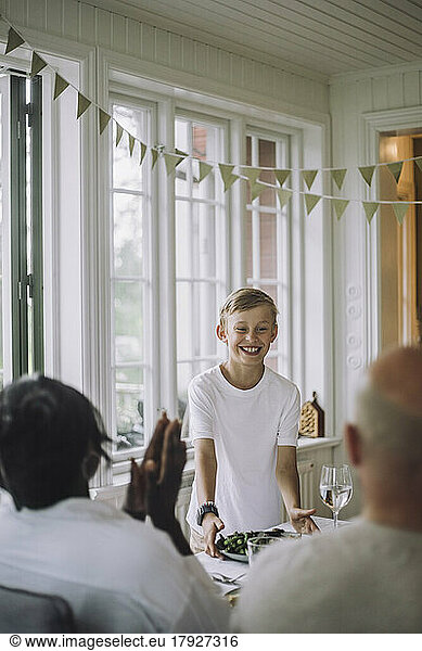 Smiling boy serving food during dinner party at home