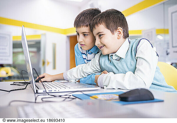 Smiling boy sharing laptop with friend at computer class in school