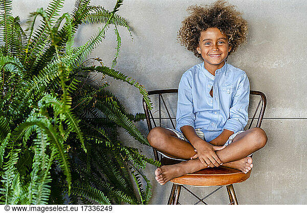 Smiling boy sitting cross-legged on chair at home