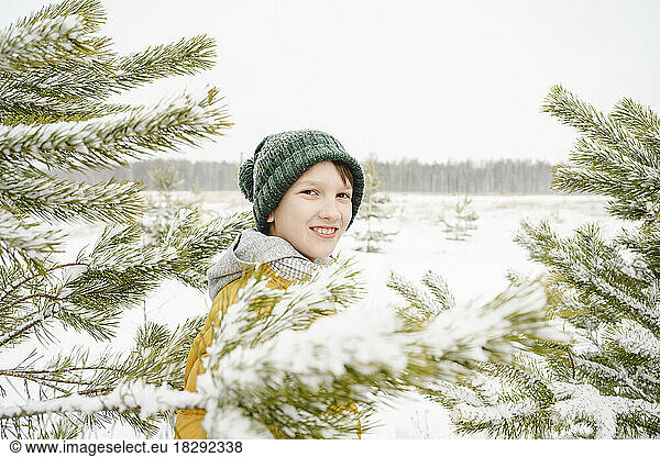 Smiling boy standing admist snow covered pine trees