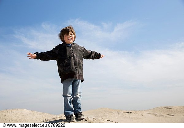 Smiling boy standing on sand with arms outstretched