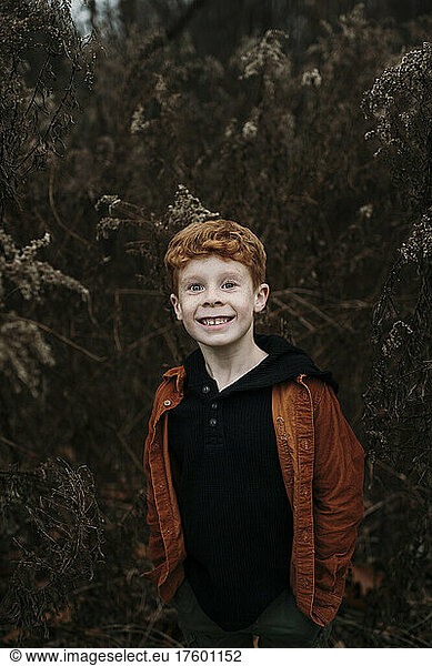 Smiling boy standing with hands in pockets in forest