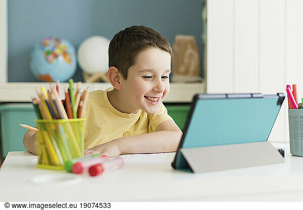 Smiling boy studying on tablet PC at home