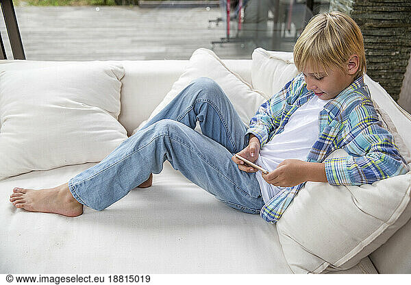 Smiling boy using smart phone on sofa at home