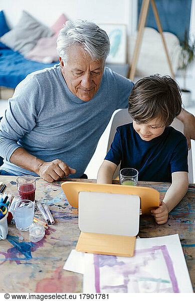 Smiling boy using tablet computer by grandfather at home