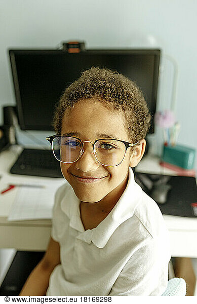 Smiling boy wearing eyeglasses in front of desktop PC at home