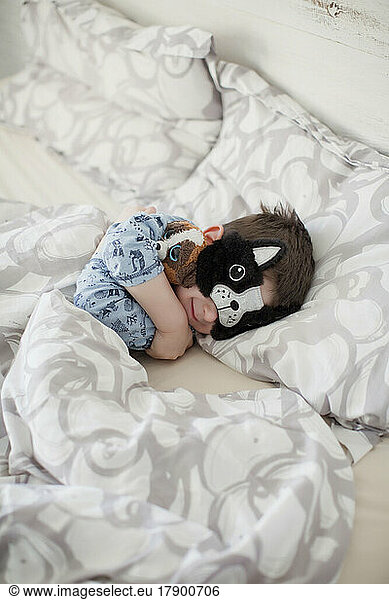 Smiling boy wearing sleep mask on bed