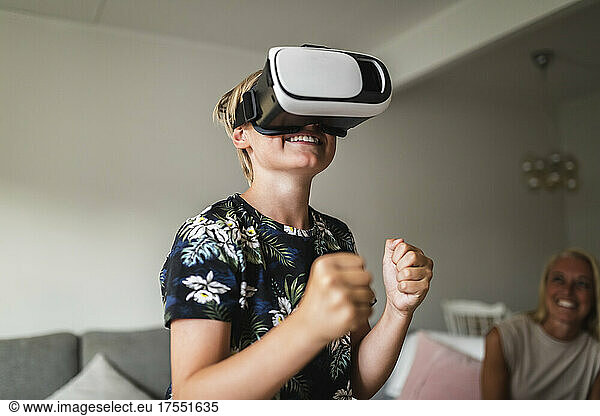 Smiling boy wearing virtual reality headset while mother sitting in background at home