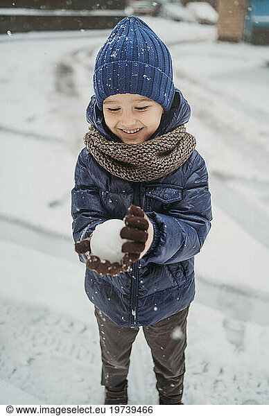 Smiling boy wearing warm clothes making snowball in winter