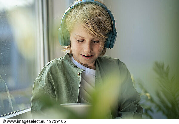 Smiling boy wearing wireless headphones and using tablet PC at home
