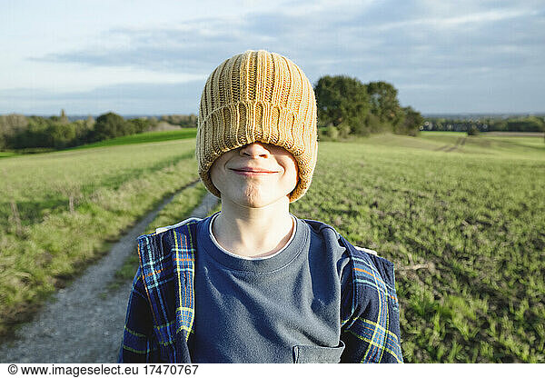 Smiling boy with eyes covered by knit hat on field