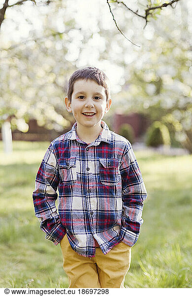 Smiling boy with hands in pockets standing at back yard