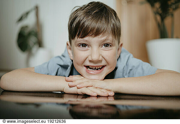 Smiling boy with head resting on arms at home