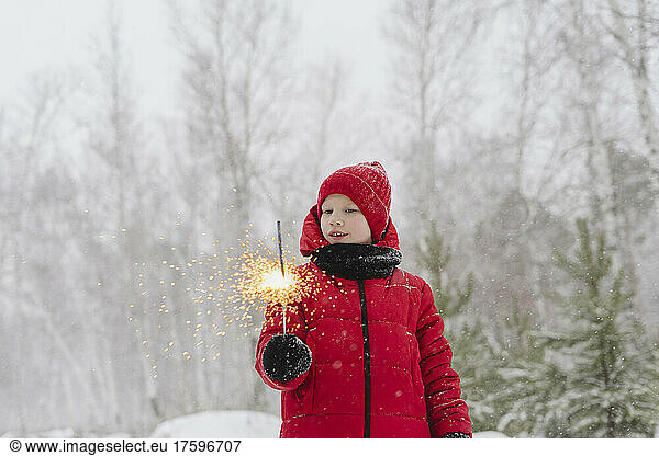 Smiling boy with sparkler in snow forest