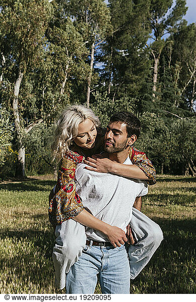 Smiling boyfriend giving piggyback ride to girlfriend in park on sunny day