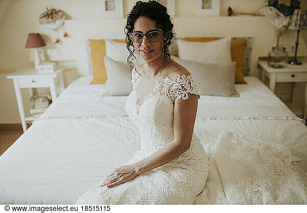 Smiling bride in wedding dress sitting on bed