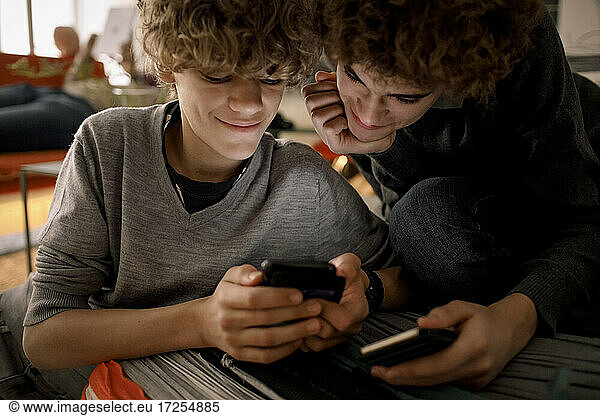 Smiling brothers sharing smart phone while sitting in living room at home