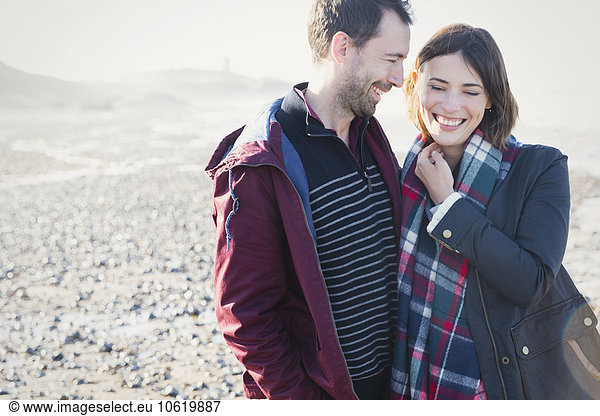 Smiling brunette couple standing on sunny rocky beach