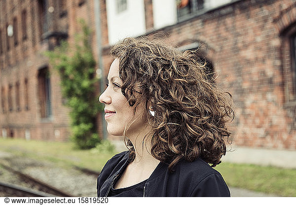 Smiling brunette woman with curly hair in front of a brick building and old rail tracks