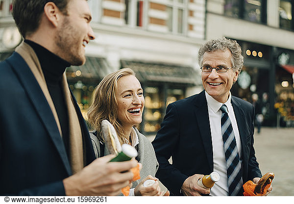 Smiling business colleagues discussing while holding food and drink in city