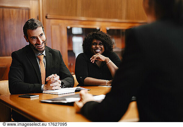 Smiling business colleagues discussing while sitting in conference room during meeting