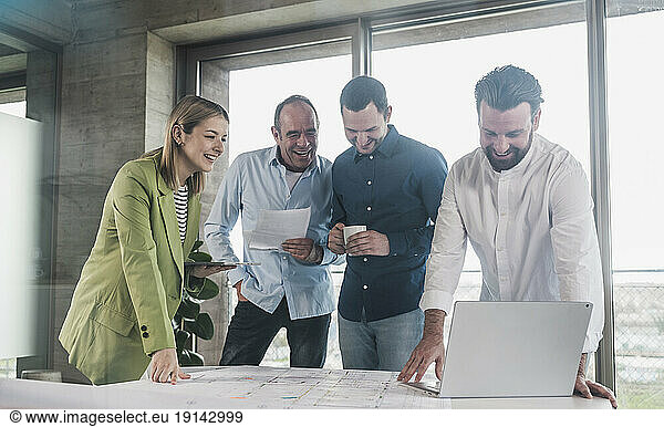 Smiling business colleagues examining blueprint at table in office