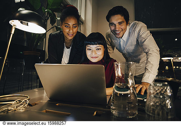 Smiling business colleagues planning strategy over laptop while working late at creative office