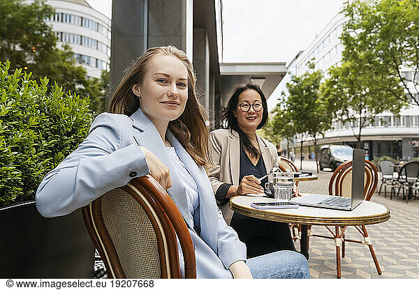 Smiling business partners sitting at table in sidewalk cafe