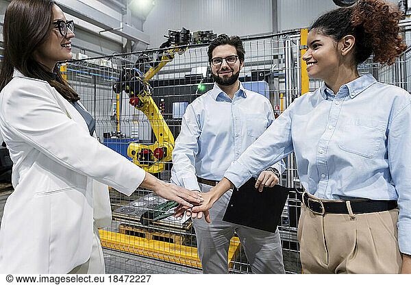 Smiling business people stacking hands in factory