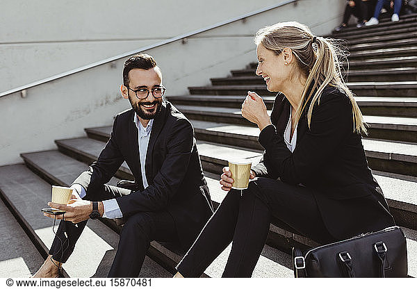 Smiling business people with coffee sitting on staircase