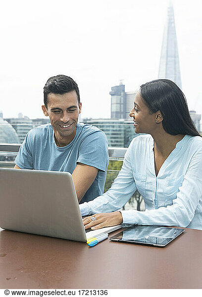 Smiling business people working at laptop on urban balcony  London  UK