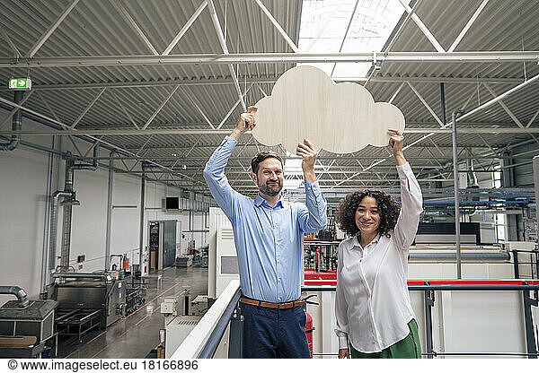 Smiling businessman and businesswoman holding cloud shaped cut out in industry