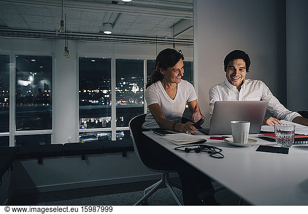 Smiling businessman and businesswoman planning strategy while looking at laptop in office