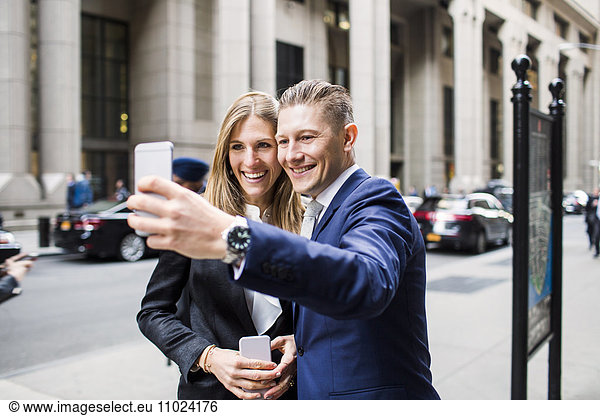 Smiling businessman and woman taking selfie while standing at city
