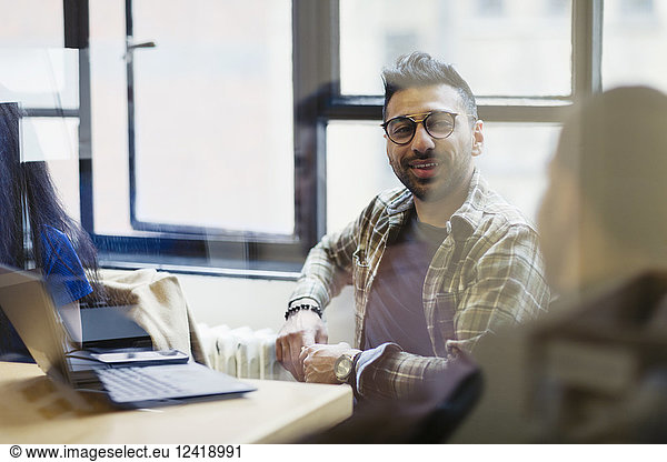 Smiling businessman at laptop talking with colleague in office meeting