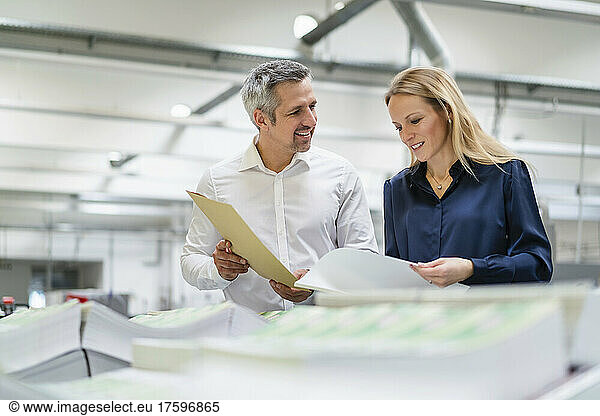 Smiling businessman discussing with colleague reading documents in factory