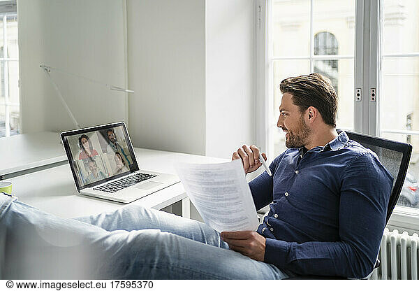 Smiling businessman discussing with colleagues in meeting on video call at office