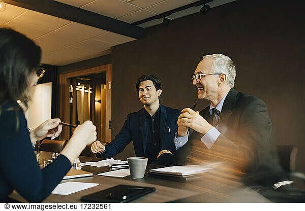 Smiling businessman discussing with male and female colleague in board room