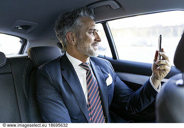Smiling businessman doing video call through smart phone sitting in car