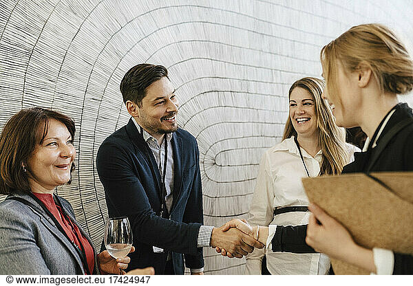 Smiling businessman greeting female professional while doing handshake during networking event