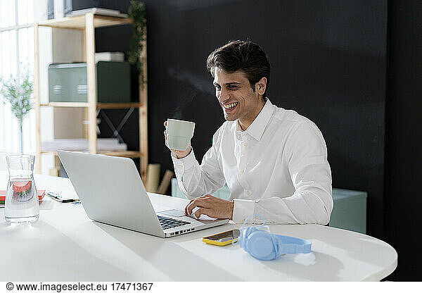 Smiling businessman having and using laptop at desk in office