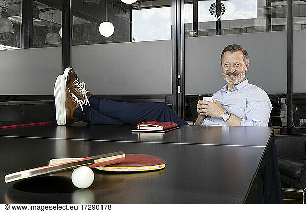 Smiling businessman having coffee while sitting at table tennis table in office