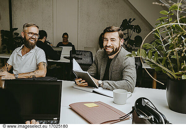 Smiling businessman holding diary while sitting with male colleague in coworking office