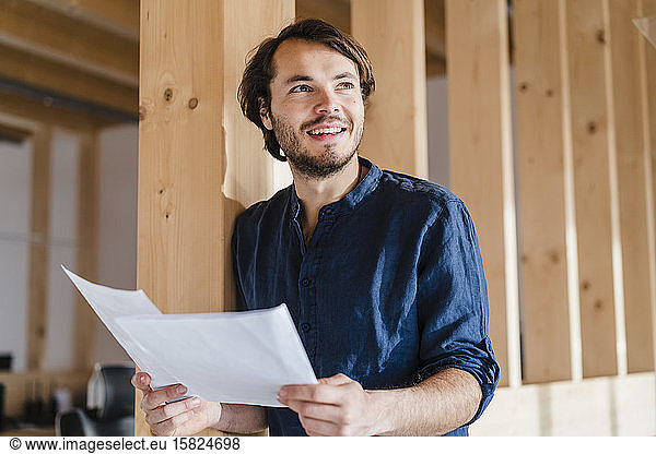 Smiling businessman holding documents in wooden open-plan office