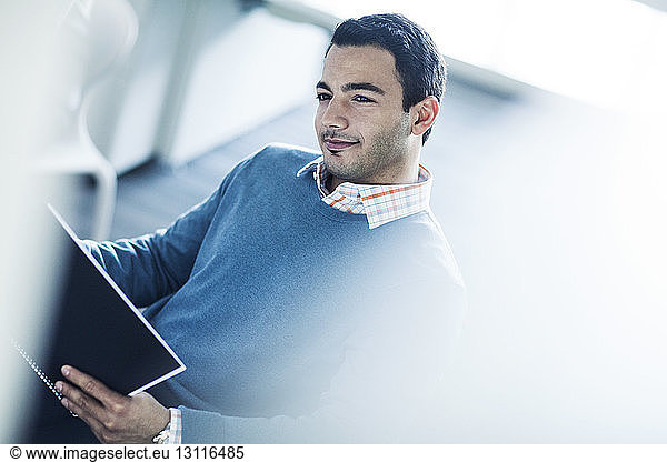 Smiling businessman holding file while sitting in office